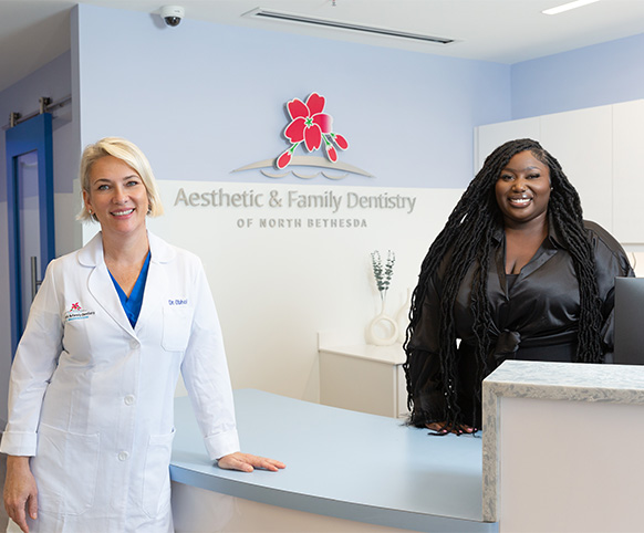 Oral surgeon and team member smiling at reception desk of dental office in North Bethesda