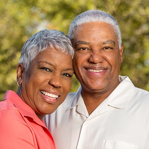 Older man and woman smiling outdoors with dental implants in North Bethesda