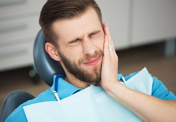 Man in dental chair holding his cheek in pain