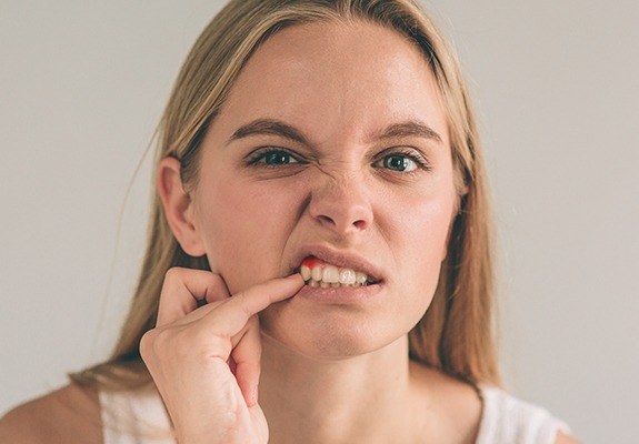 Woman pointing to red inflammed gum tissue before oral pathology appointment
