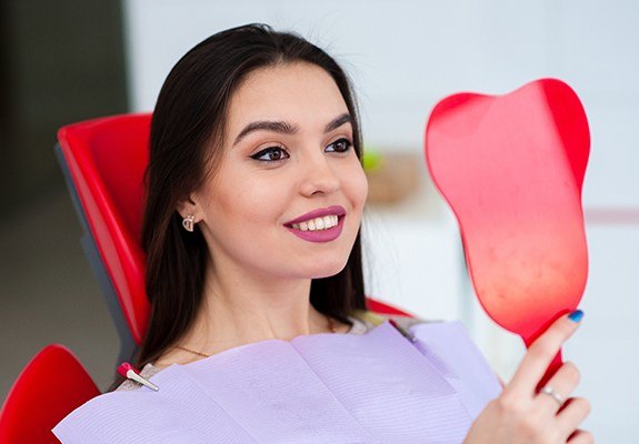 Woman looking at smile in hand mirror after facial cosmetic surgery